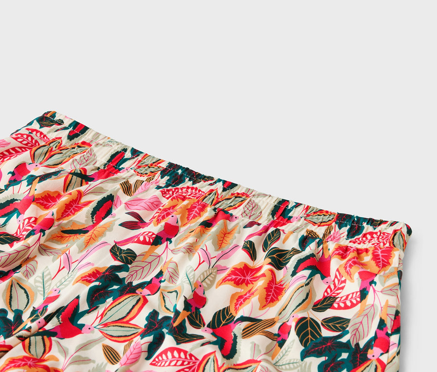 Nahaufnahme vom Bund einer Hose mit einem Muster aus Blättern und Vögeln in Rot-, Rosa-, Grün- und Orangetönen.