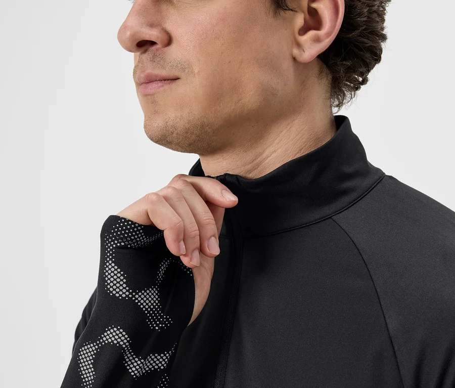 Mann öffnet den Reißverschluss eines schwarzen Langarmshirts mit gepunkteten Ärmeln.