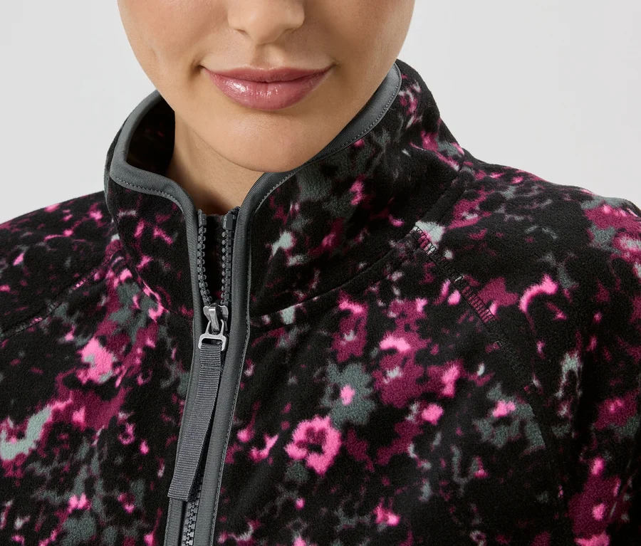 Nahaufnahme einer Frau, die eine Fleecejacke mit Reißverschluss und Blumenmuster in Pink und Grau trägt.