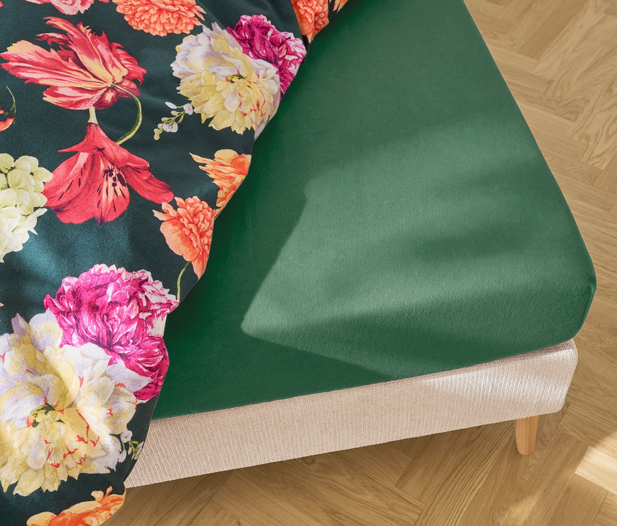 Bett mit dunkelgrünem Spannbettlaken und dunkelgrüner Bettwäsche mit Blumenmuster.