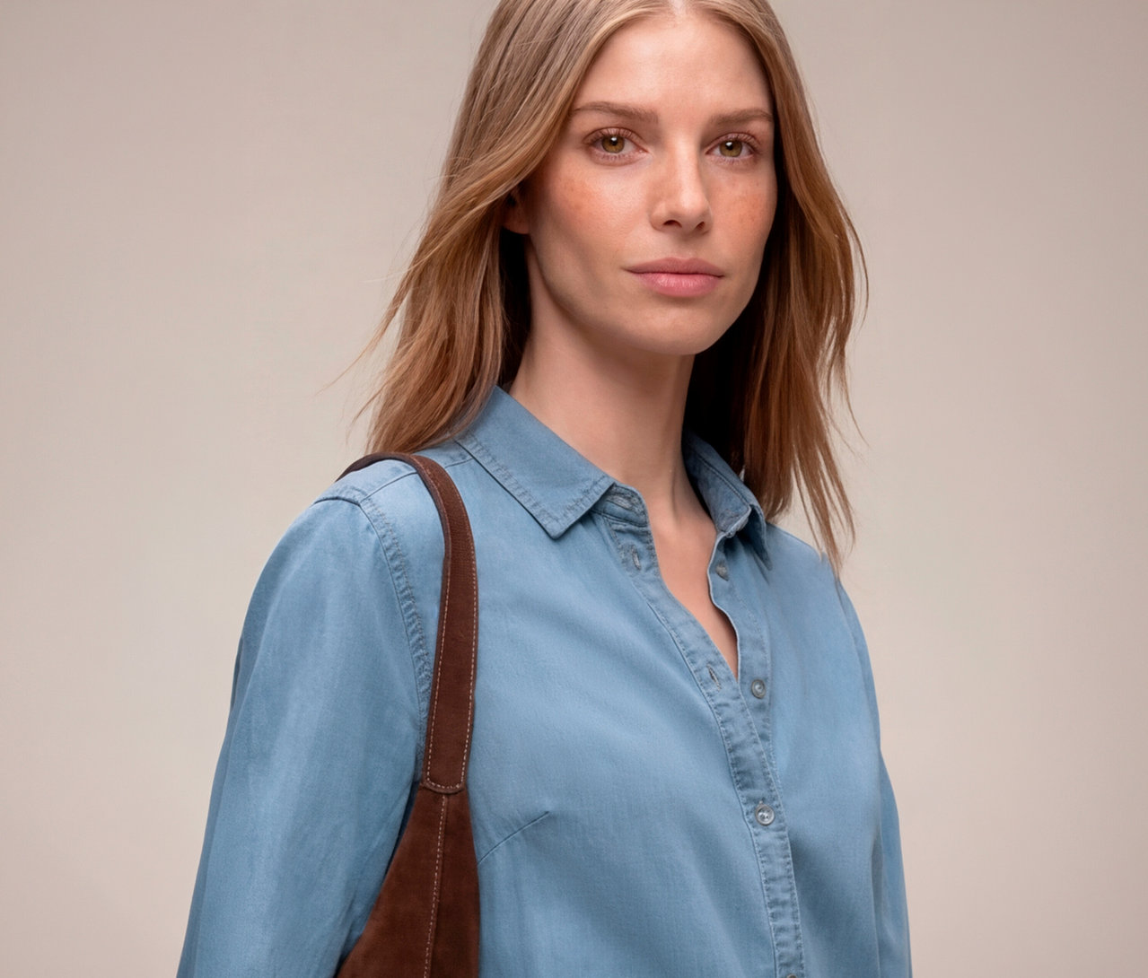 Frau mit hellbraunem Haar und hellblauem Jeanshemd, braune Tasche über der Schulter.