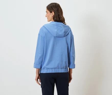 Frau trägt einen hellblauen Kapuzenpullover und marineblaue Hosen, von hinten gesehen.