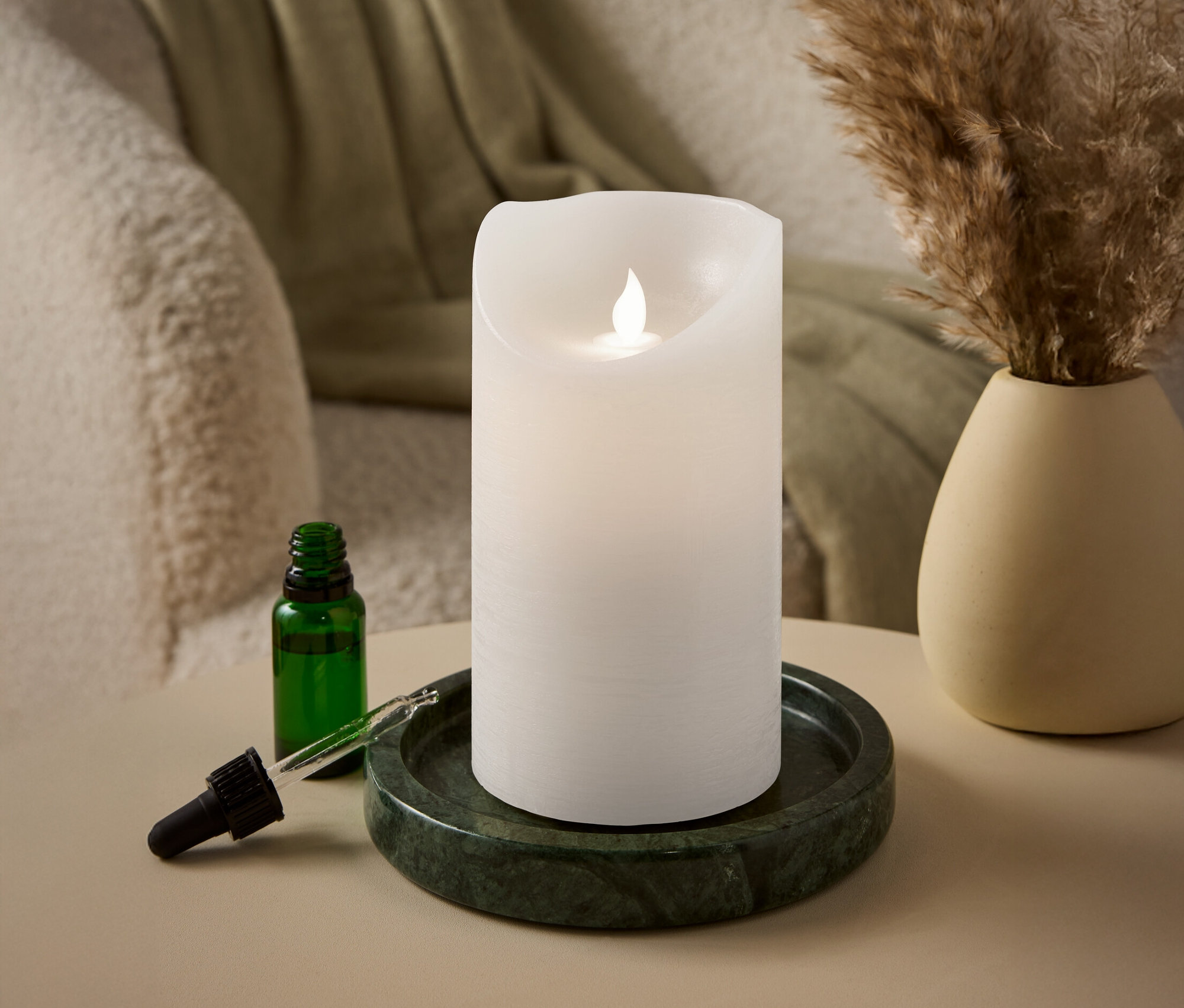 Eine weiße Stumpenkerze mit LED-Flamme steht auf einem grünen Marmortablett neben einer grünen Glasflasche mit Pipette.