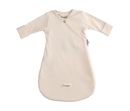 Cremefarbener Babyschlafsack mit langen Ärmeln, Wickelverschluss oben mit Druckknopf und seitlichem Reißverschluss. Unten ist das "Sterntaler"-Logo sichtbar.