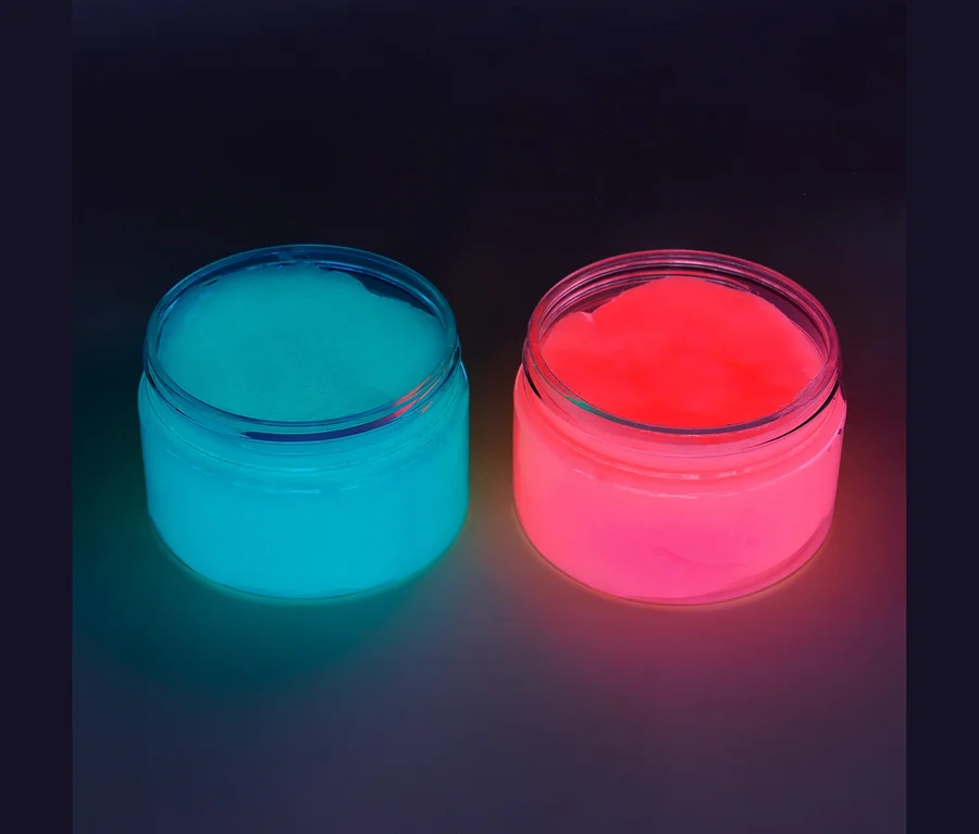 Zwei offene Gläser mit leuchtendem Schleim, eines türkisblau und eines pink, stehen nebeneinander auf dunklem Untergrund.