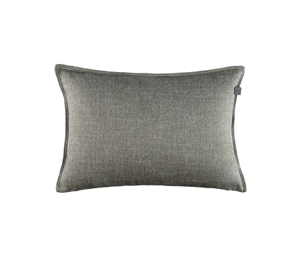 Rechteckiges Kissen in Grau-Beige mit strukturierter Oberfläche und kleinem dunklen Etikett oben rechts.