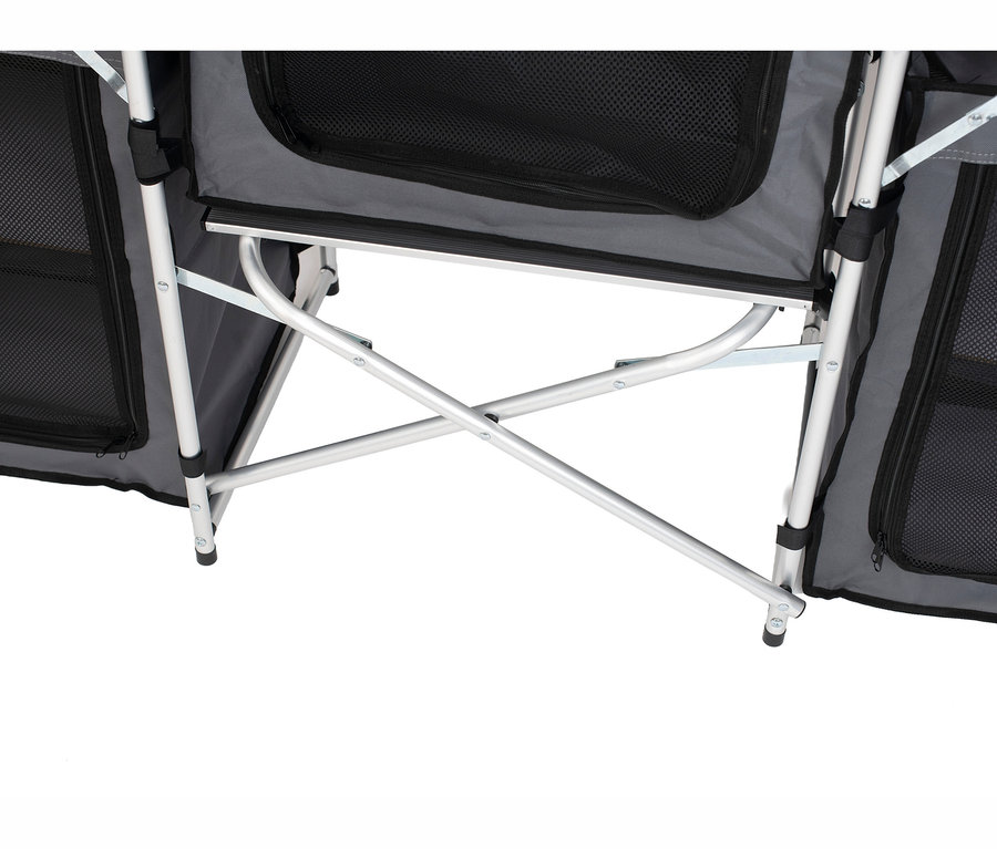 Nahaufnahme des unteren Bereichs einer faltbaren Campingküche »Redwood M«, die ihr silbernes Aluminiumgestell mit X-förmigen Stützstangen und graue Stofffächer mit schwarzen Netzreißverschlüssen zeigt. Schwarze Füße sind unten sichtbar.
