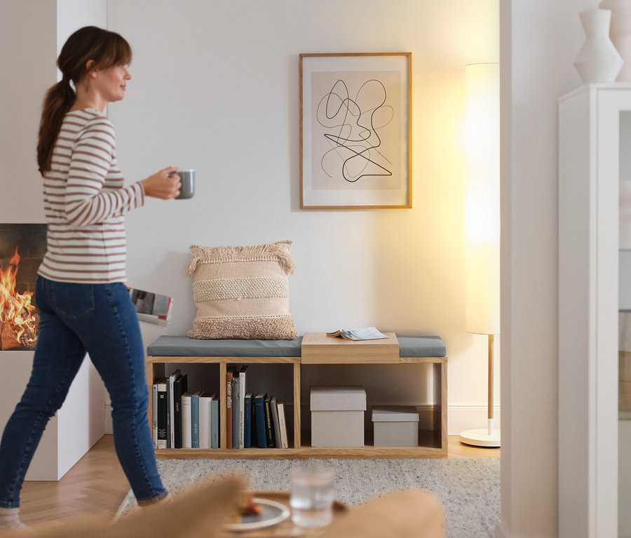 Frau geht mit Tasse an der Sitzbank mit Polster vorbei.