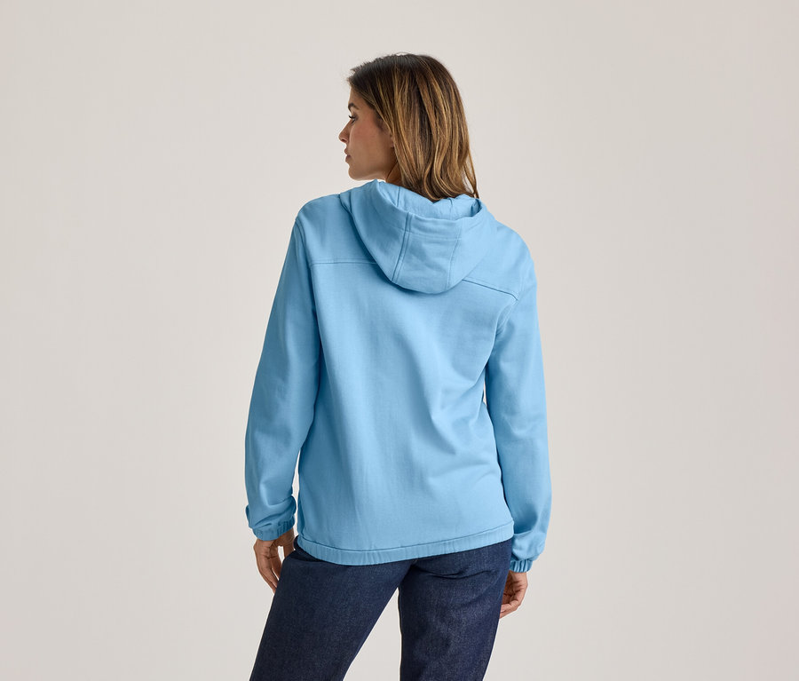 Frau von hinten in hellblauer Kapuzenjacke und dunkler Jeans, blickt nach rechts.