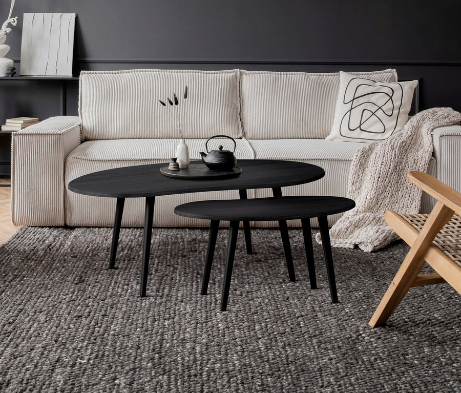 Wohnzimmer mit beigem Cordsofa, davor zwei schwarze ovale Eglo Tische »ALORAN« auf einem grauen Teppich. Auf dem größeren Tisch stehen eine Teekanne und eine Vase.