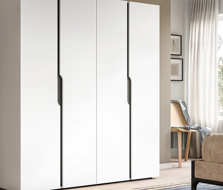 Großer weißer viertüriger Kleiderschrank mit dunklen Griffmulden in einem modernen Raum. Rechts sind ein Fenster mit weißen Vorhängen, ein Holzstuhl, ein Bett und ein Nachttisch mit Lampe zu sehen.