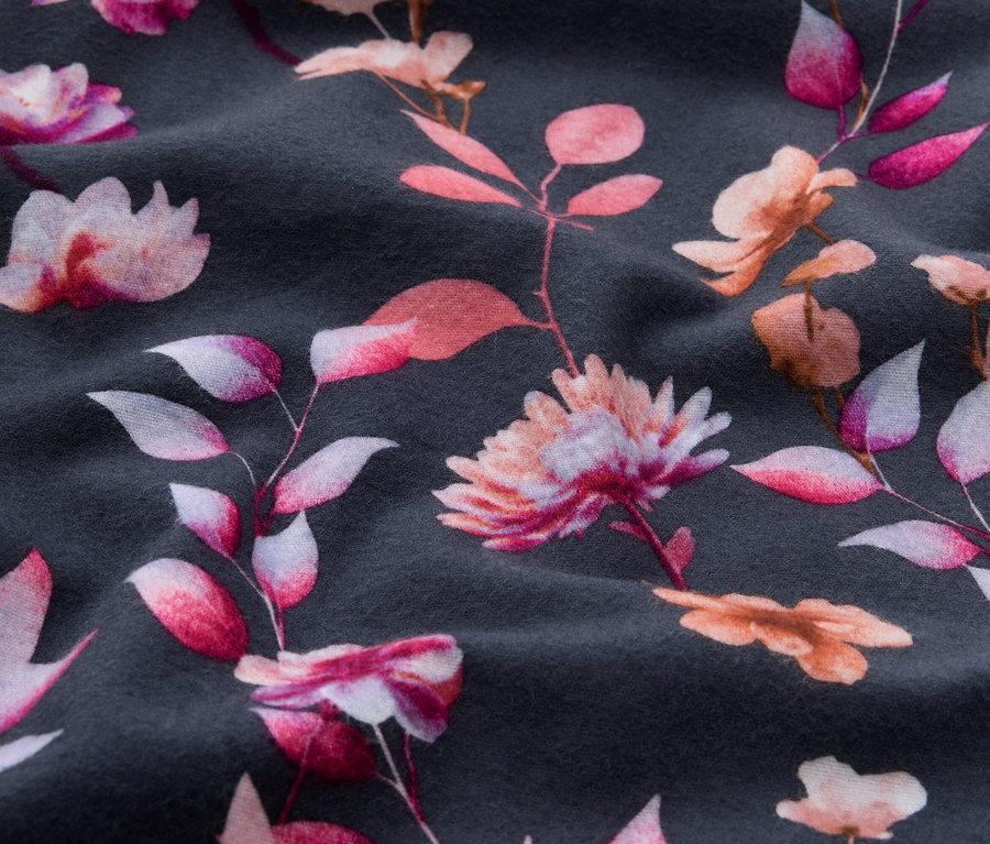 Dunkelgrauer Stoff mit Blumenmuster aus rosa, fuchsiafarbenen und pfirsichfarbenen Blüten und Blättern, der weiche Falten zeigt.