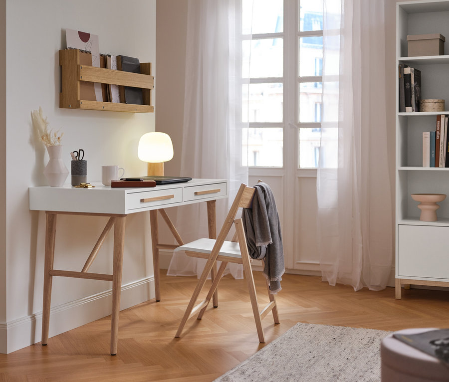 Ein weißer Sekretär »Eklund« mit Schubladen steht neben einem Stuhl an der Wand.