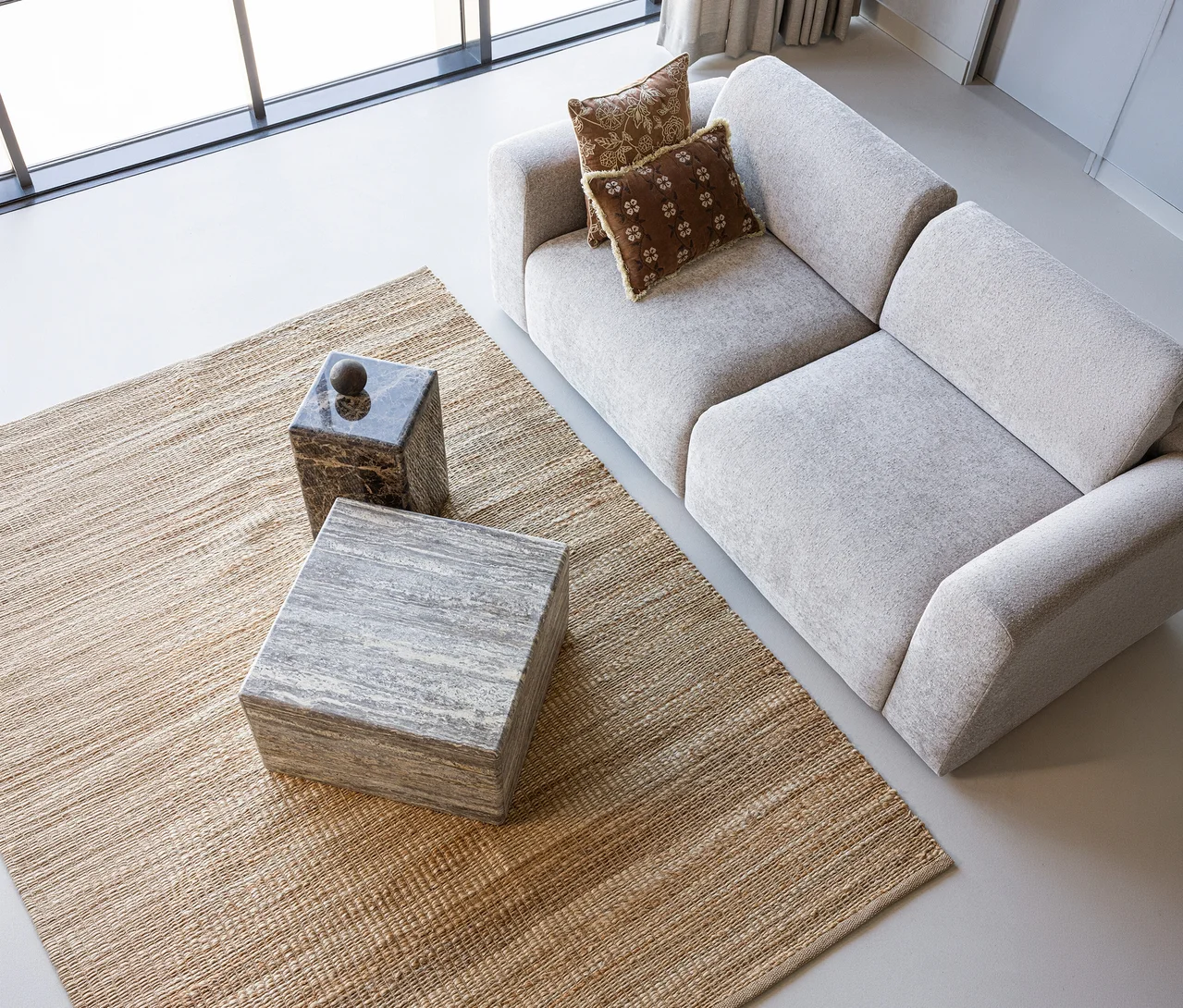 Heller WOOOD Teppich »Tepas« unter einem grauen Sofa mit zwei braunen Kissen und zwei Beistelltischen in einem modernen Raum.