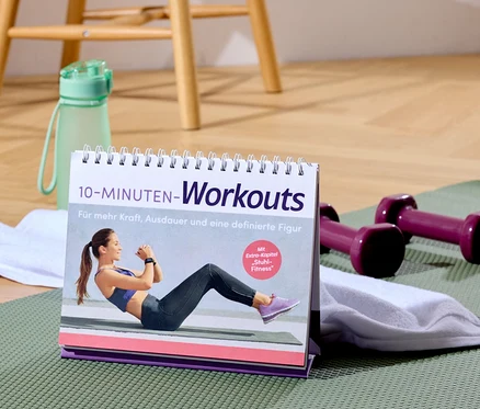 Auf einer Trainingsmatte liegen ein Kalender mit der Aufschrift 10-MINUTEN-Workouts, daneben lila Hanteln, ein Handtuch und eine Wasserflasche.