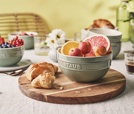 Frühstückstisch mit einer eukalyptusfarbenen STAUB Keramik-Schüssel (ca. 12 cm) gefüllt mit Obst, einer weiteren Schüssel mit Beeren und Croissants auf einem Holzbrett.