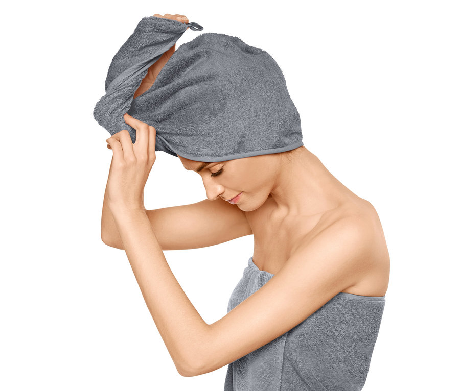 Frau setzt Turban-Handtuch auf den Kopf, Körper mit Handtuch umwickelt.