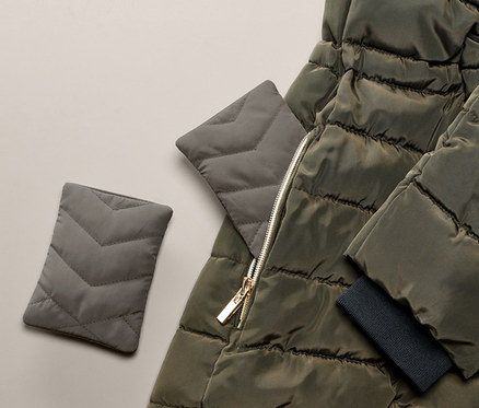 Zwei Taschen-Heizkissen liegen neben einer olivgrünen Steppjacke.