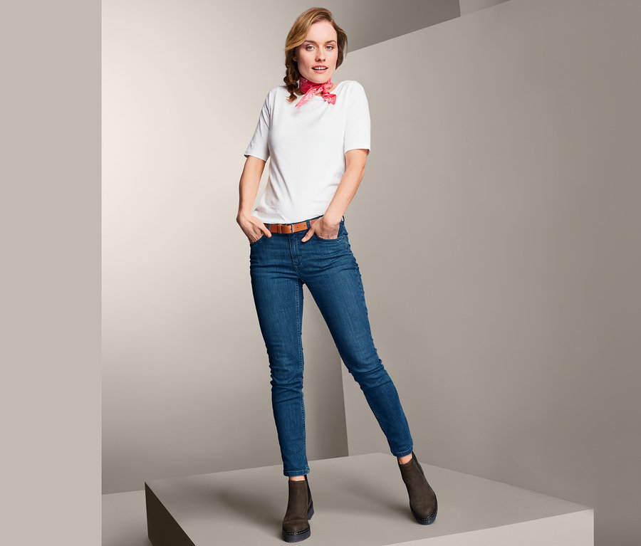 Frau posiert auf Podest in Slimfit-Jeans, weißem T-Shirt und braunen Schuhen.