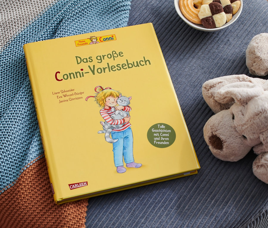 Auf einem blauen Hocker liegen das gelbe Buch »Das große Conni-Vorlesebuch«, ein Plüschhund, eine Schale Kekse und eine Strickdecke.