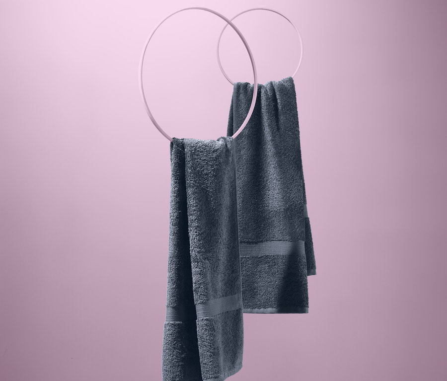 Zwei graue Frottier-Handtücher, 2 Stück, hängen an runden Halterungen vor einem rosa Hintergrund.