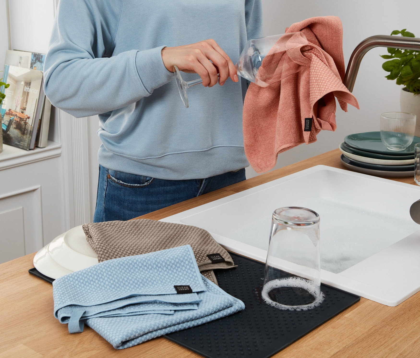 Frau trocknet ein Glas mit einem rosa Geschirrtuch aus dem 3er-Set ab.