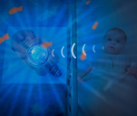 Säugling liegt im Kinderbett, daneben ZAZU-Ozeanprojektor »Otto«.