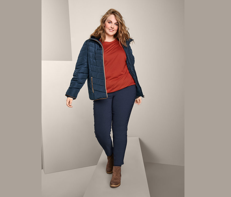 Eine Frau geht auf einem Laufsteg und trägt eine Steppjacke, ein Kurzarmshirt mit Stickerei und eine Bengalin-Hose.