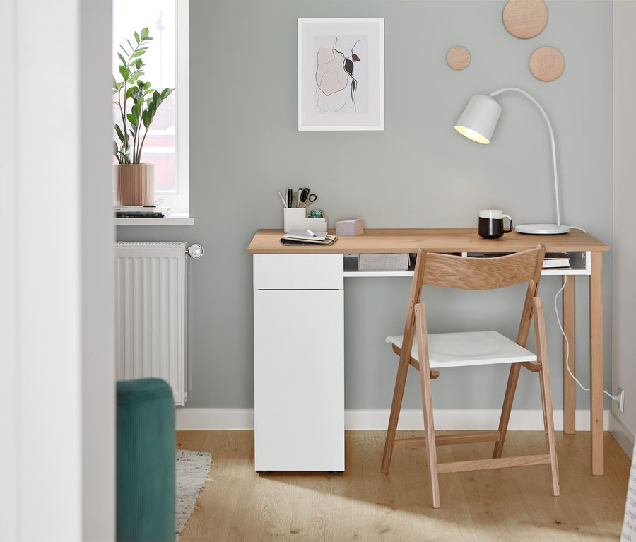 Klappstuhl aus FSC®-zertifiziertem Eschenholz steht an einem Schreibtisch. Auf dem Schreibtisch steht eine Tischleuchte aus Metall, weiß.