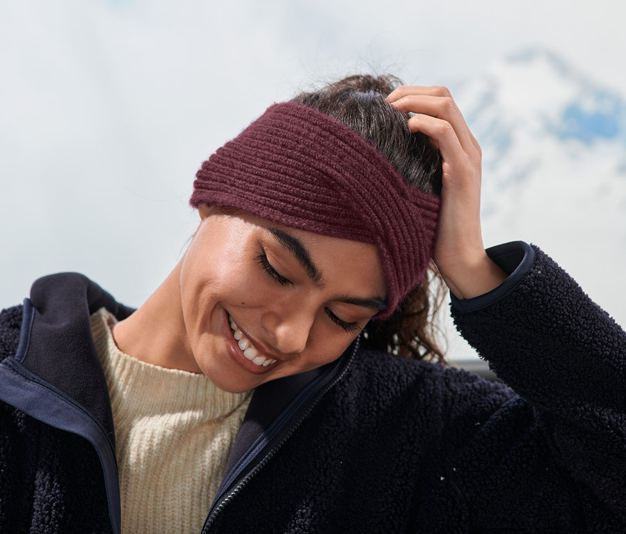 Frau lächelt und trägt ein bordeauxrotes Strick-Stirnband.