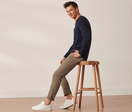 Mann sitzt auf einem Holzhocker und trägt eine sandfarbene Chino.