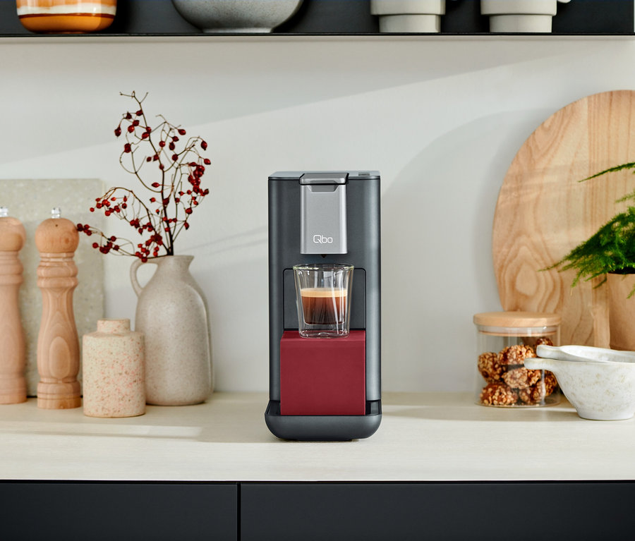 Eine Qbo ESSENTIAL Dark Berry Kaffeemaschine mit einer Tasse Kaffee auf einer Küchentheke.