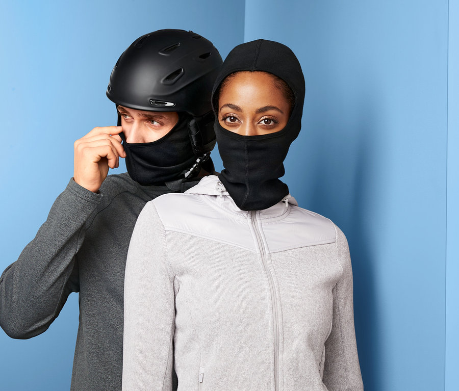Mann justiert schwarze Performance-Sturmhaube unter schwarzem Skihelm, daneben Frau mit schwarzer Performance-Sturmhaube und grauem Fleece.