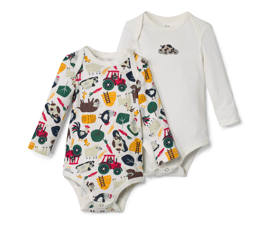 Zwei Baby-Langarmbodys liegen übereinander. Ein Body ist weiß mit einem Tierbild, der andere ist mit Traktoren, Tieren und Pflanzen bedruckt.