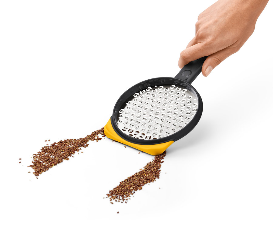 Eine Hand hält eine 2-seitige Schnellreibe und reibt Samen auf eine weiße Oberfläche.