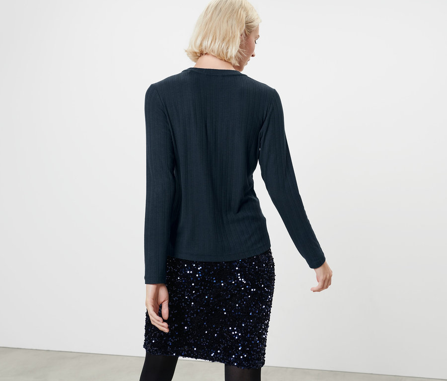 Frau von hinten trägt ein dunkelblaues Langarmshirt und einen Paillettenrock.