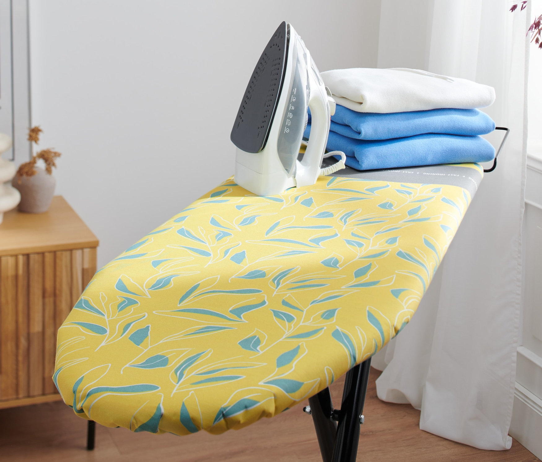Bügeleisen steht auf Bügelbrett mit Bügelbrettbezug.