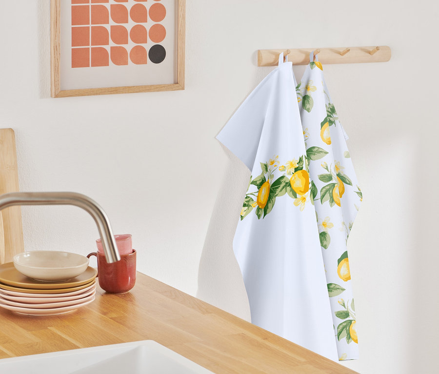 Zwei Geschirrtücher mit Zitronenmuster hängen an einer Holzleiste.