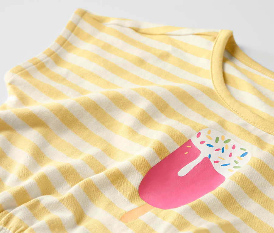 Detailaufnahme eines Kinder-Jumpsuits mit gelben Streifen und Eis am Stiel-Motiv.