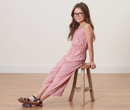 Mädchen sitzt auf einem Hocker und trägt einen Kinder-Web-Jumpsuit in 7/8-Länge.