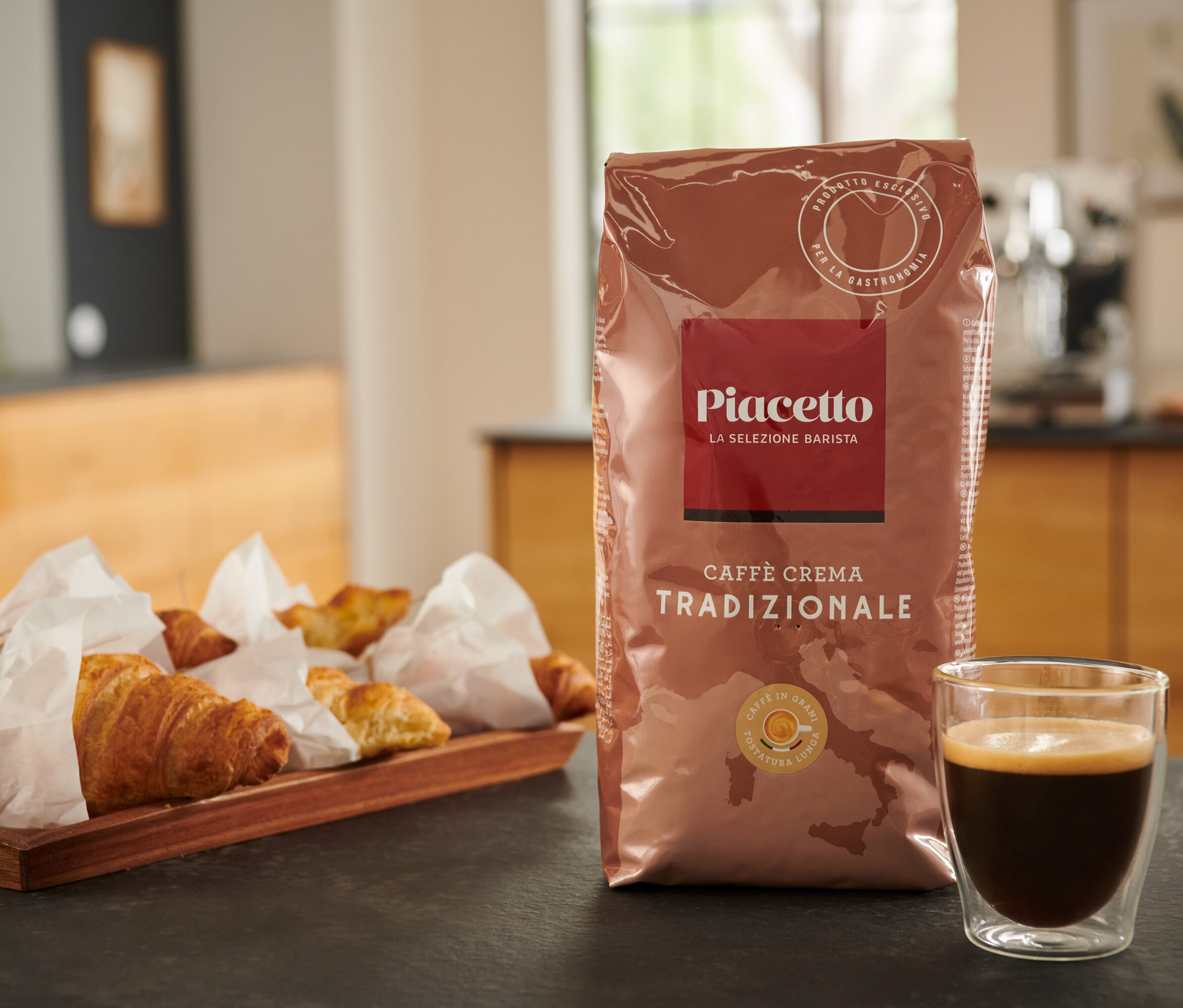 Eine Packung Piacetto Caffè Crema Tradizionale, Kaffee und Croissants auf einem Tisch.
