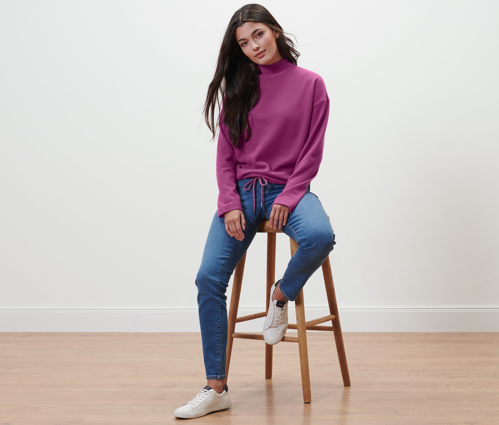 Frau sitzt auf einem Hocker und trägt ein violettes Sweatshirt mit Stehkragen.