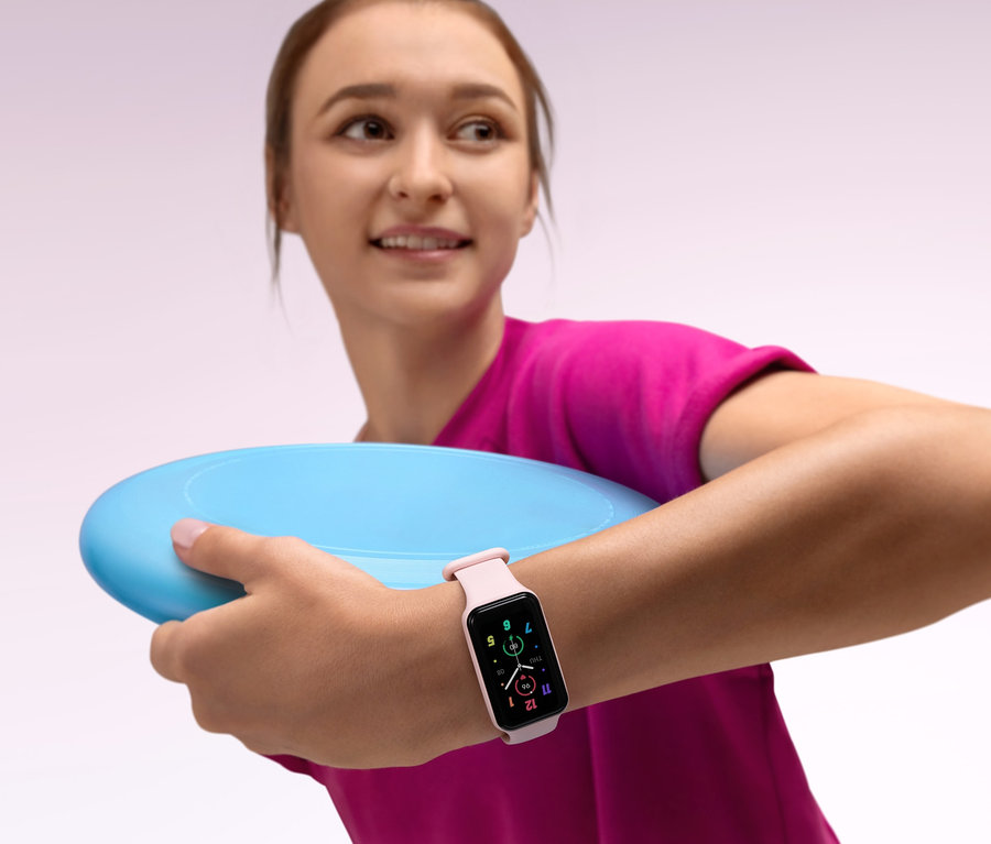 Junge Frau hält eine hellblaue Frisbee in der Hand und trägt ein rosa Amazfit Band 7 Aktivitätstracker am Handgelenk.