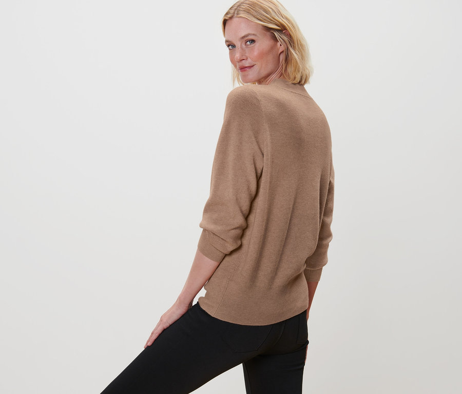 Frau blickt über die Schulter und trägt einen Strickpullover und eine schwarze Hose.
