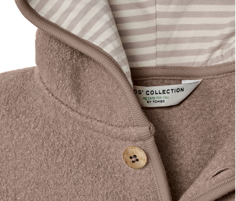 Detailansicht einer Kinder-Walkjacke mit Merinowolle, mit Kapuze mit beige- und weiß gestreiften Innenfutter und Knopfverschluss.