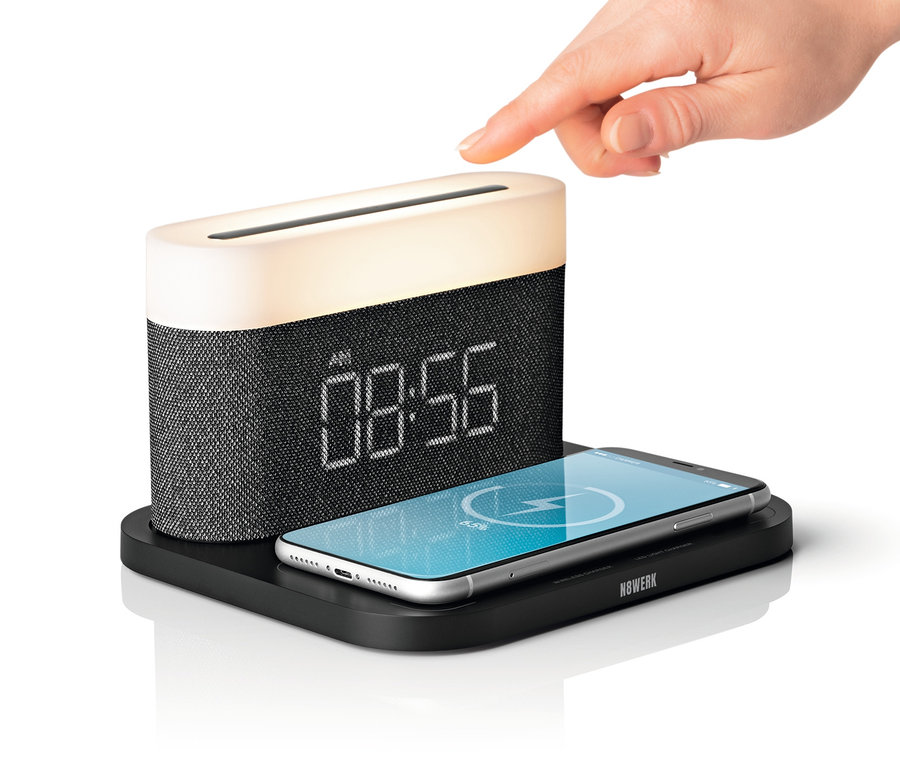 Eine Hand berührt den schwarzen N8WERK Nachttischlampen-Wecker mit Wireless Charger, auf dem ein Smartphone liegt.