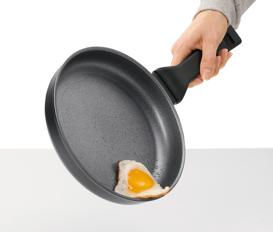 Hand hält eine Profi-Aluminium-Pfanne mit Spiegelei.