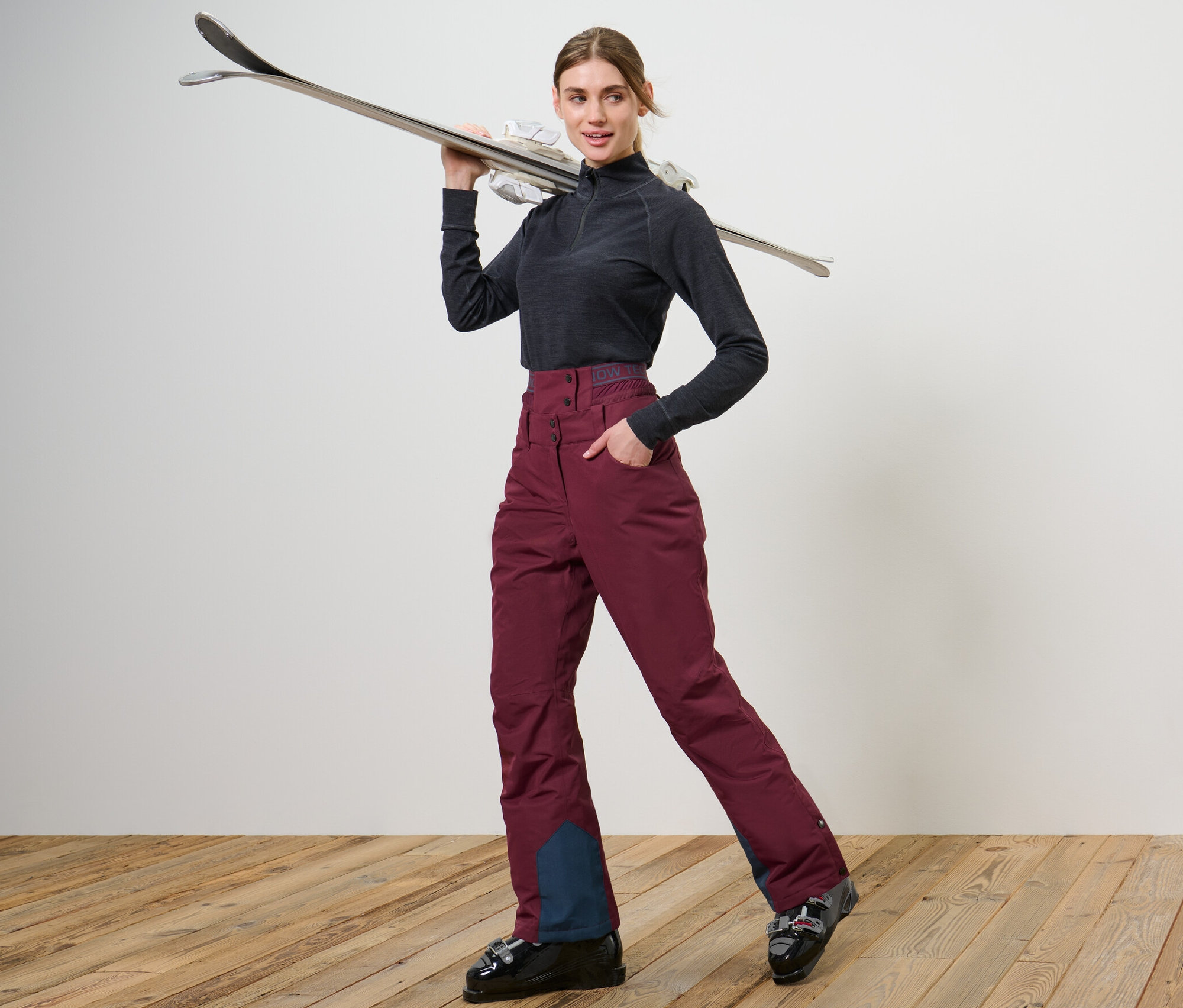 Frau posiert in Skischuhen und weinroten Ski- und Snowboardhose.