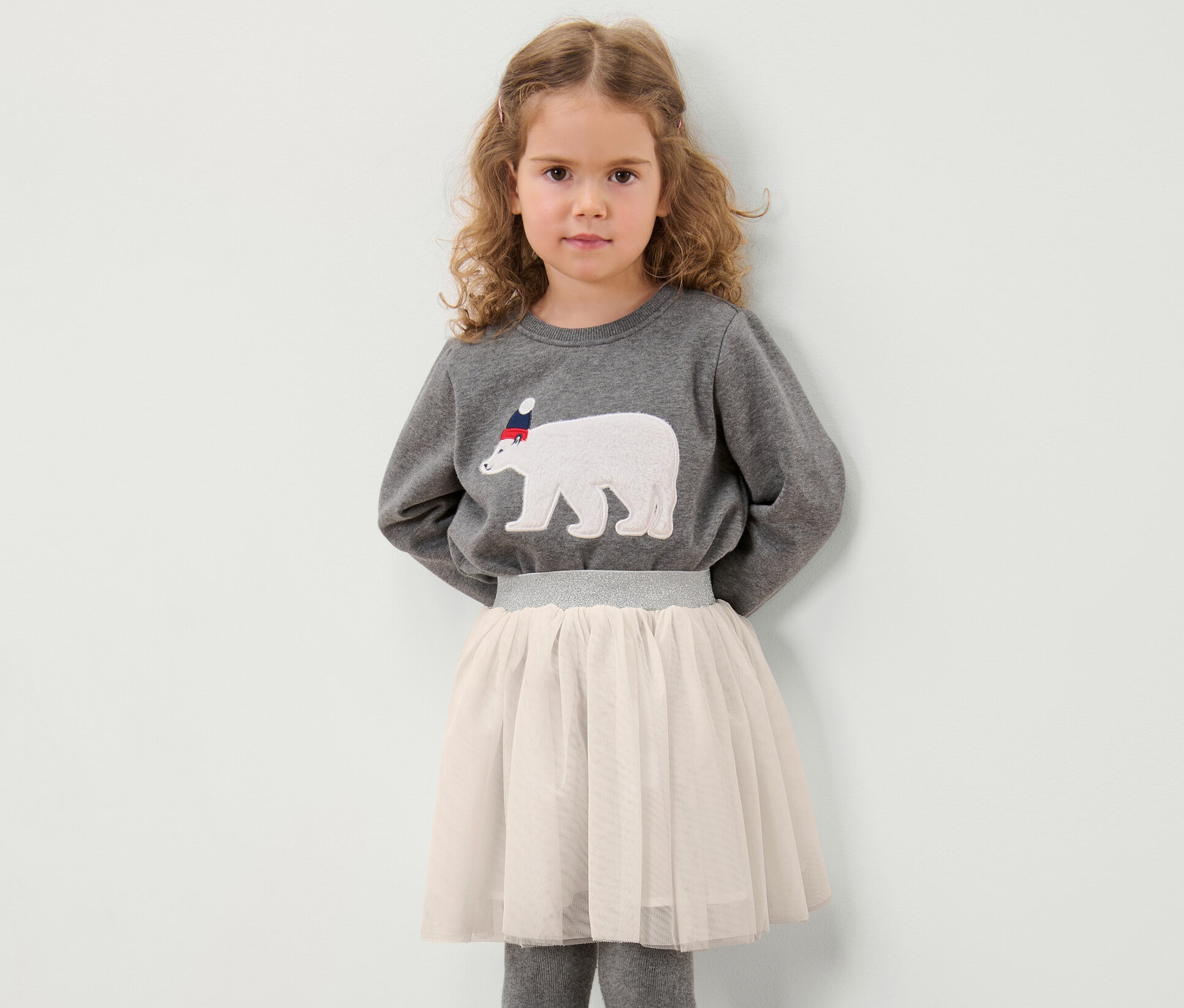 Mädchen posiert in grauem Sweatshirt mit Eisbär-Motiv und Kinder-Tüllrock.