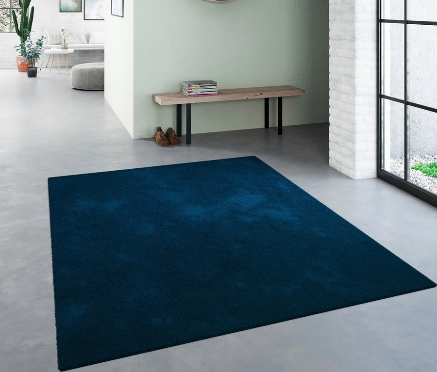 Eingangsbereich mit blauem Teppich "Mellow", Bank, Schuhen und rundem Spiegel.